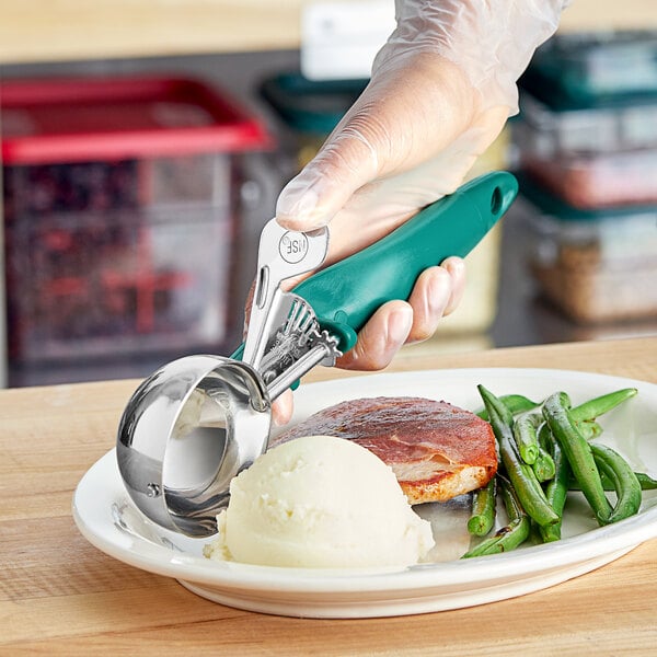 A person holding a green Choice Ergonomic thumb press ice cream scoop full of food.
