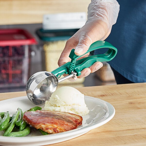 A person using a green EZ Grip ice cream scoop to scoop a dish of ice cream.