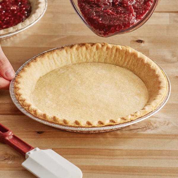 A person using a spatula to put red jam in a Chef Pierre unbaked pie shell.