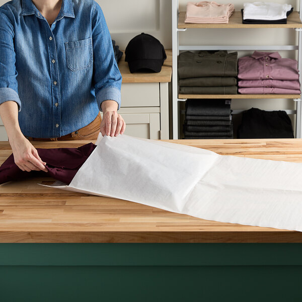 A person folding brown pants into a white Vela paper layflat bag.