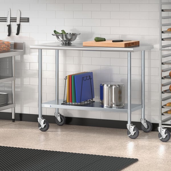 A Steelton stainless steel work table with undershelf and casters in a kitchen with rolling carts and shelves.