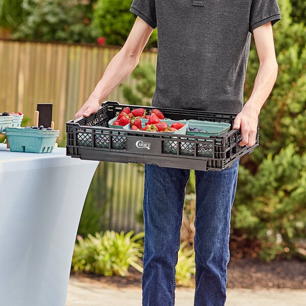 A man holding a Choice black vented collapsible crate of strawberries.