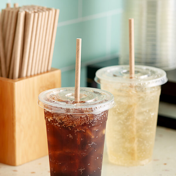 Two plastic cups with Aardvark paper straws filled with brown liquid on a counter.