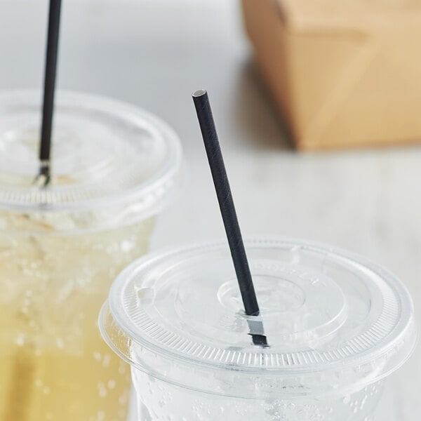 A couple of plastic cups with Aardvark black unwrapped paper straws in them on a table.