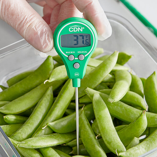 A person using a green CDN digital pocket probe thermometer to measure peas.