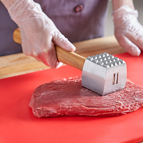 A person holding a Vollrath meat hammer over a meat block.
