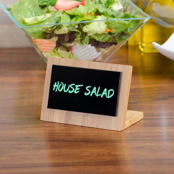 A Cal-Mil bamboo framed write on board with the words "house salad" on it on a table next to a bowl of salad.