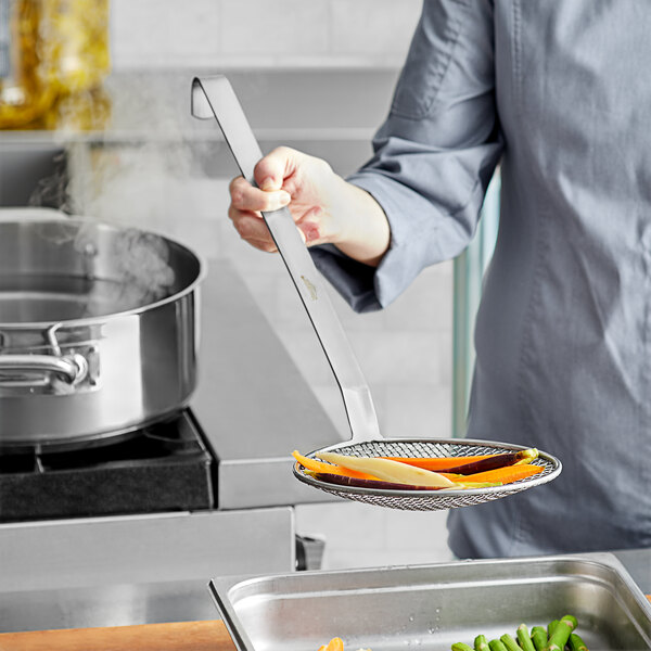 A chef using a Vollrath wire mesh skimmer over a pan.
