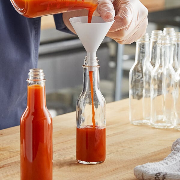 A person pouring orange liquid into a Glass Woozy Bottle.