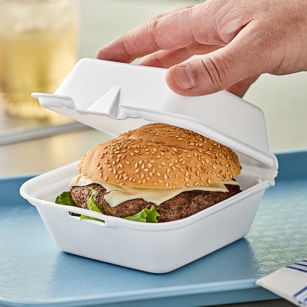 A hand holding a hamburger in a Genpak white foam container.