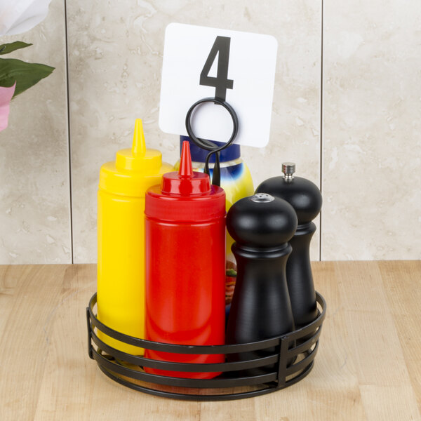 An American Metalcraft black wrought iron condiment caddy with a number card on a table with condiments.
