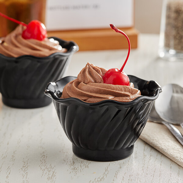 Two black plastic dessert dishes filled with chocolate mousse and topped with a cherry.