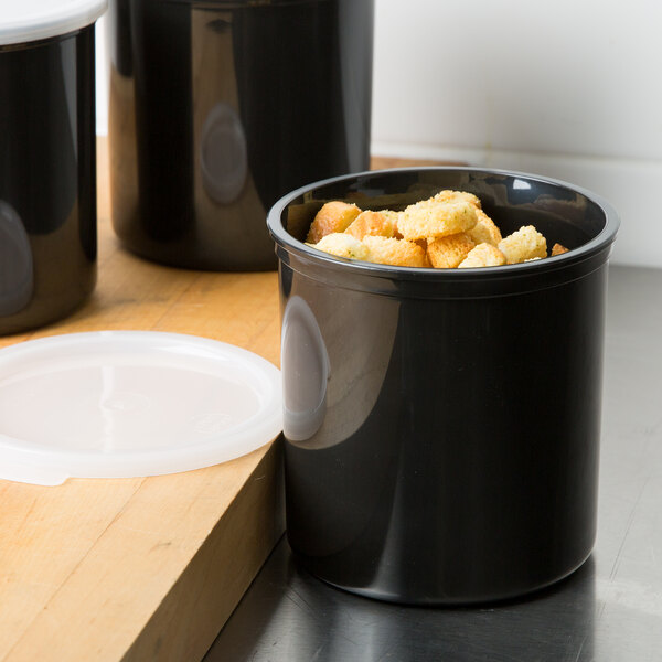 A black Cambro round polypropylene crock with a lid full of croutons.
