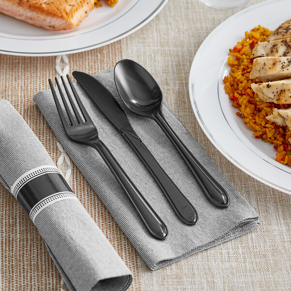 A Hoffmaster CaterWrap Onyx Gray napkin with a black plastic fork, spoon, and knife on it next to a plate of food.