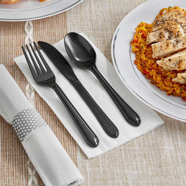 A white napkin with a black plastic fork and spoon, and a black plastic knife on a plate of rice and chicken.