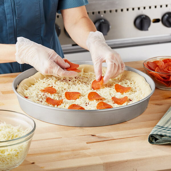 A woman using a Choice aluminum deep dish pizza pan to make a pizza.