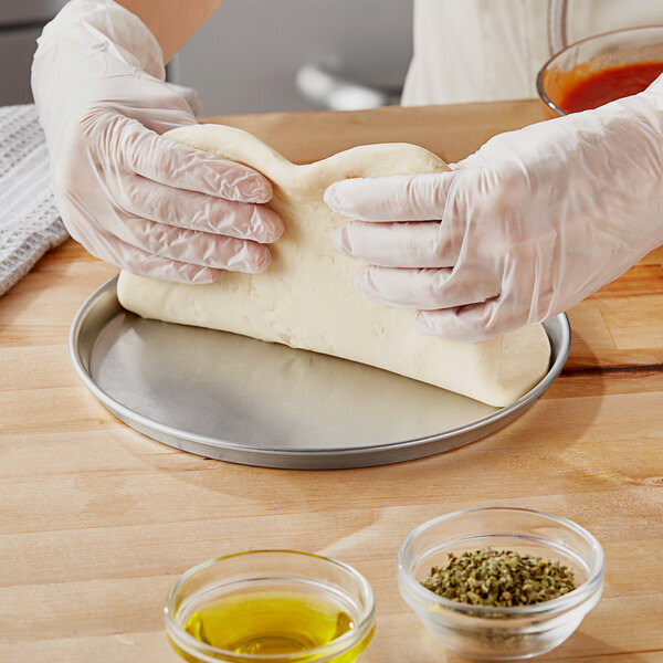 A person in gloves using a Choice aluminum pizza pan to hold pizza dough.