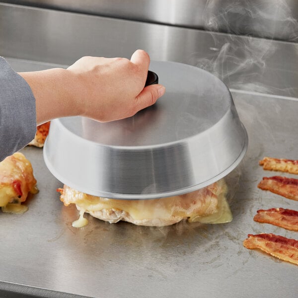 A person using the Choice 8" Round Aluminum Basting Cover to cook bacon in a pan.