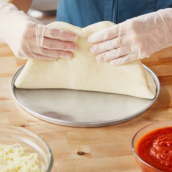 A person in gloves holding a dough on a Choice aluminum pizza pan.