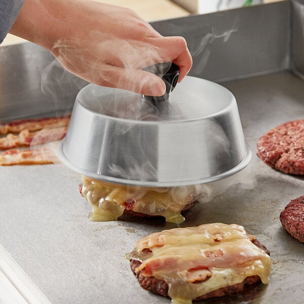 A person using a Choice aluminum basting cover to cook hamburgers on a pan.