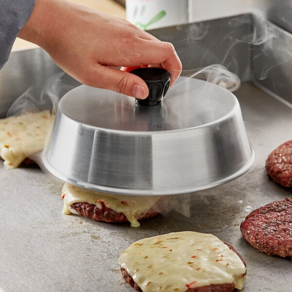 A person using a Choice aluminum basting cover to cook burgers on a pan.