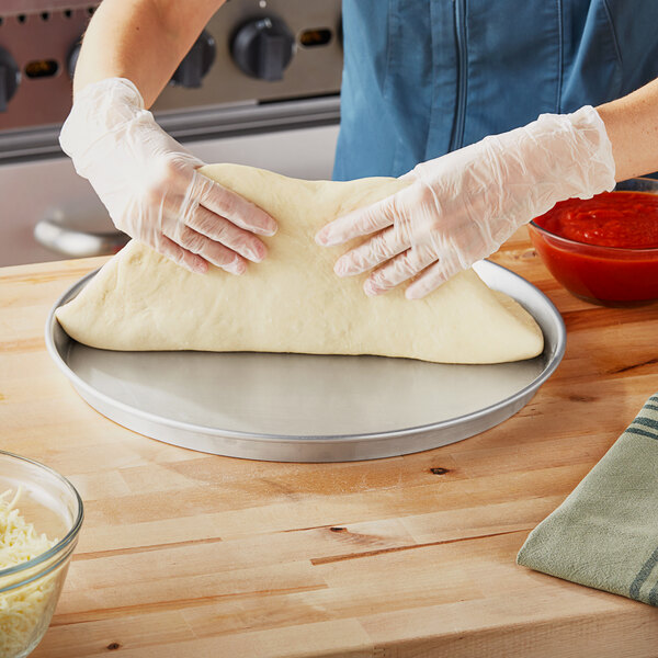 A person's hands in gloves making dough on a Choice aluminum deep dish pizza pan.