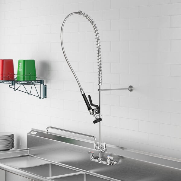 A Regency wall-mounted pre-rinse faucet with a hose attached to it above a stainless steel sink.