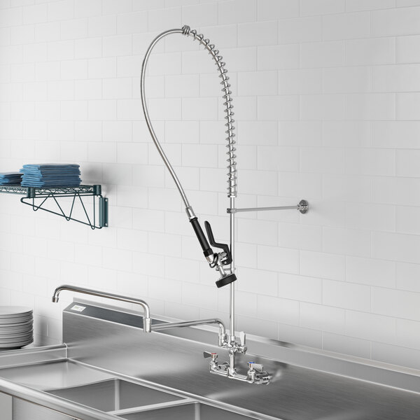 A stainless steel sink with a Regency wall-mounted pre-rinse faucet over it and a hose.