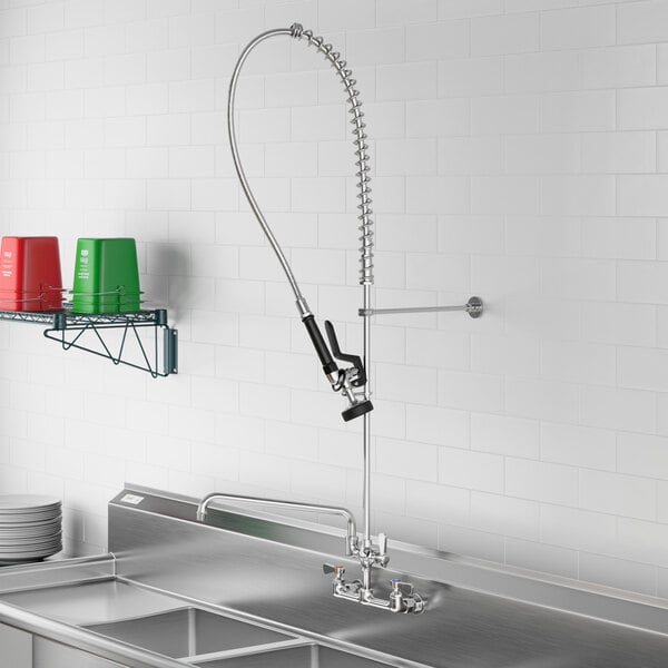 A Regency stainless steel wall-mounted pre-rinse faucet over a sink with a hose attached.