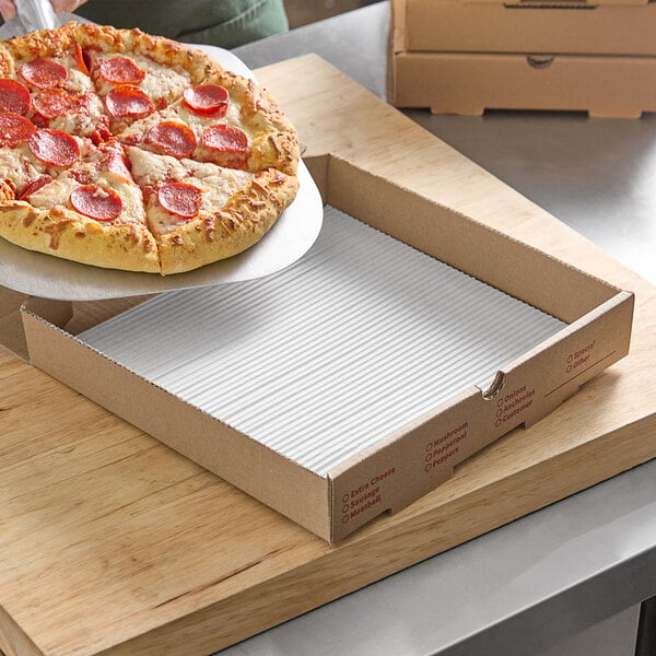 A pepperoni pizza being placed on a corrugated pad in a pizza box.
