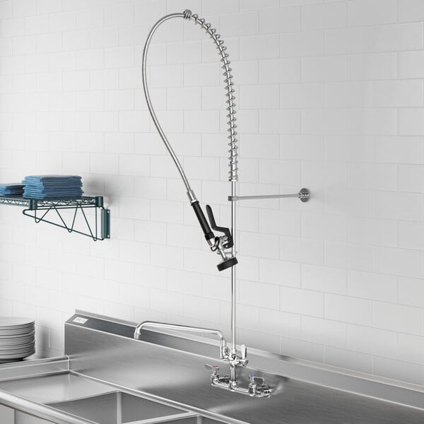 A Regency wall-mounted pre-rinse faucet over a stainless steel sink.