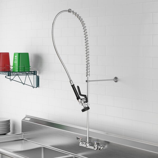 A Regency wall-mounted pre-rinse faucet over a sink with a hose attached.