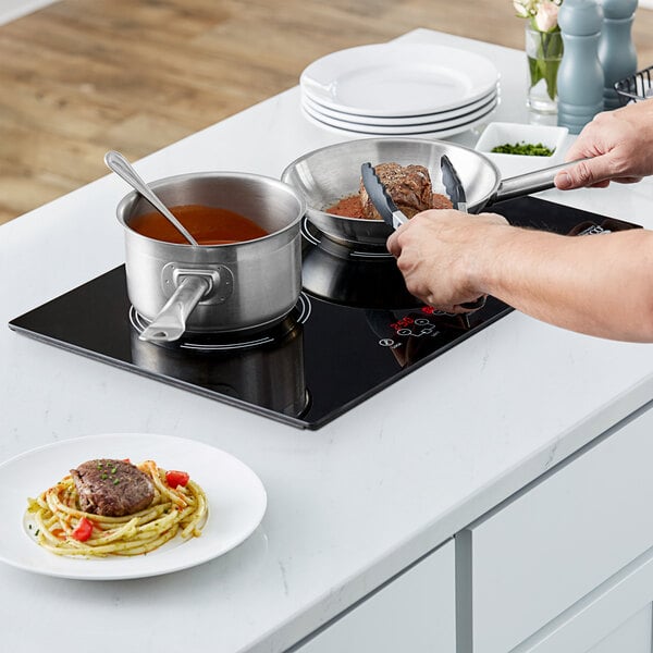 A woman cooking food on an Avantco countertop induction range.