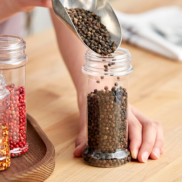 A person pouring black peppercorns into a round plastic jar.