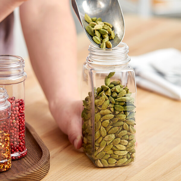 A person pouring pumpkin seeds into a rectangular plastic spice jar.