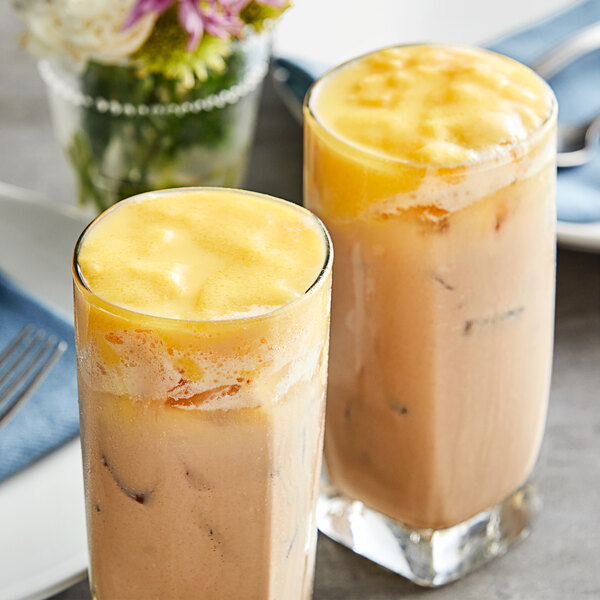 Two glasses of yellow Fanale egg pudding drinks on a table with flowers.