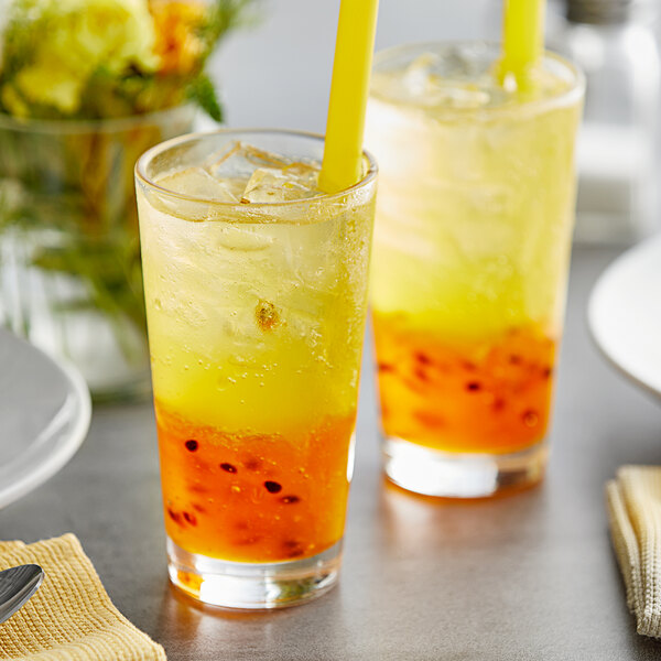 Two glasses of yellow Fanale Passion Fruit drinks with straws on a table.