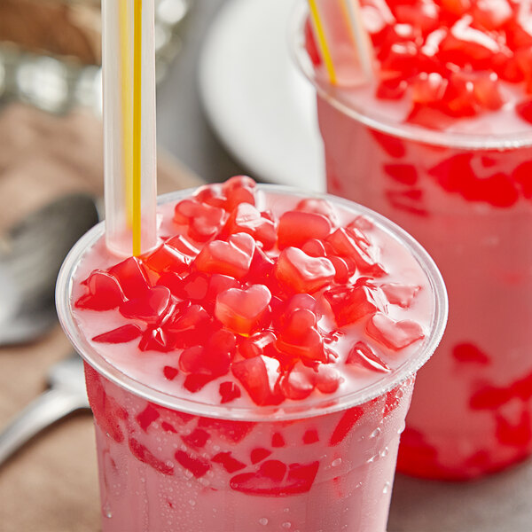 Two plastic cups of pink drinks with red jelly hearts and straws.
