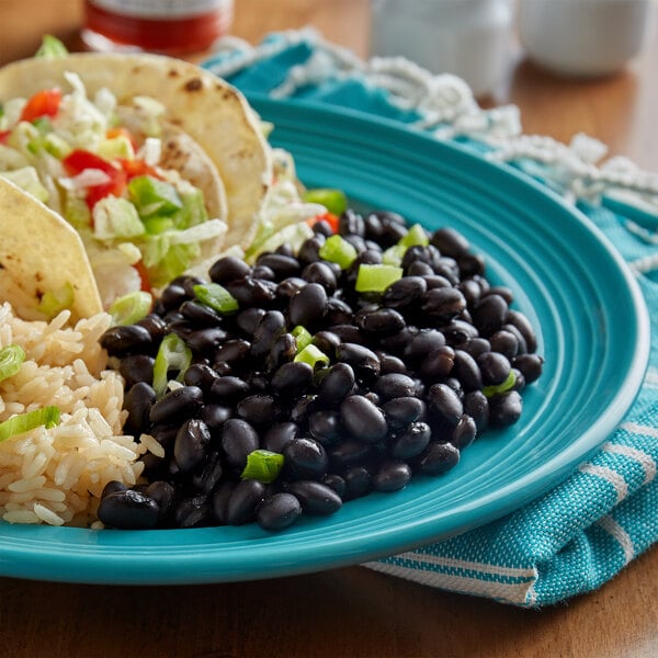 A #10 can of Furmano's Fancy Black Beans in Brine on a table with a plate of rice and beans.