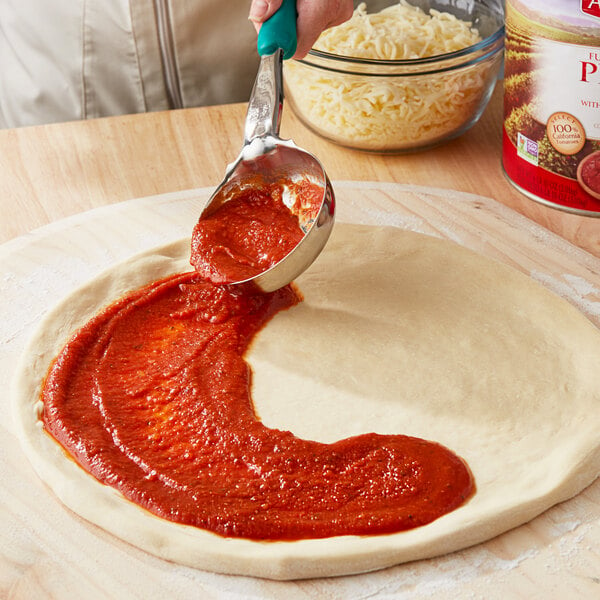 A person pouring Angela Mia pizza sauce from a spoon onto pizza dough.