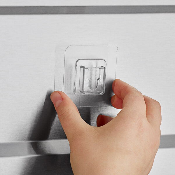 A hand using a plastic adhesive mount to open a door with a metal surface.