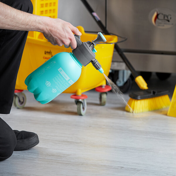 A person using a Lavex handheld pressure sprayer to clean a floor.