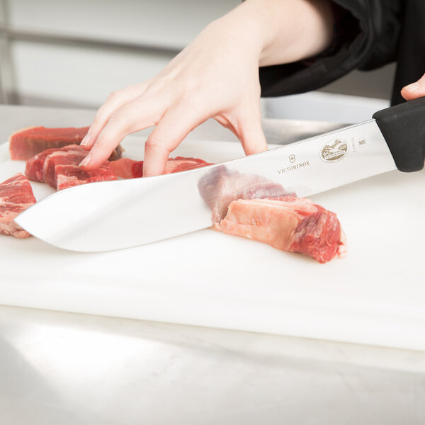 A person using a Victorinox Butcher Knife to cut meat on a cutting board.