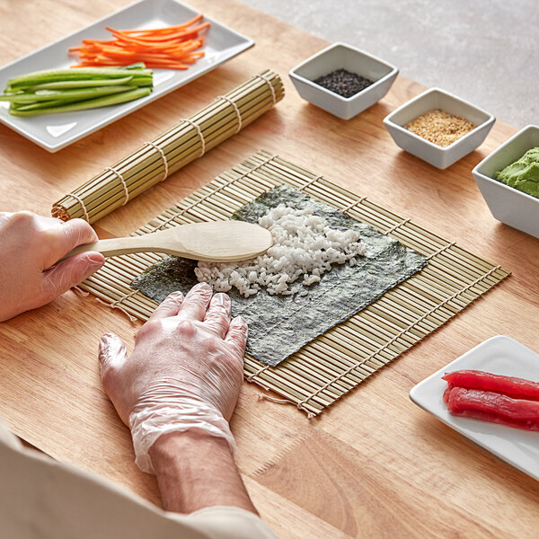 A person making sushi on a table using a bamboo sushi mat.