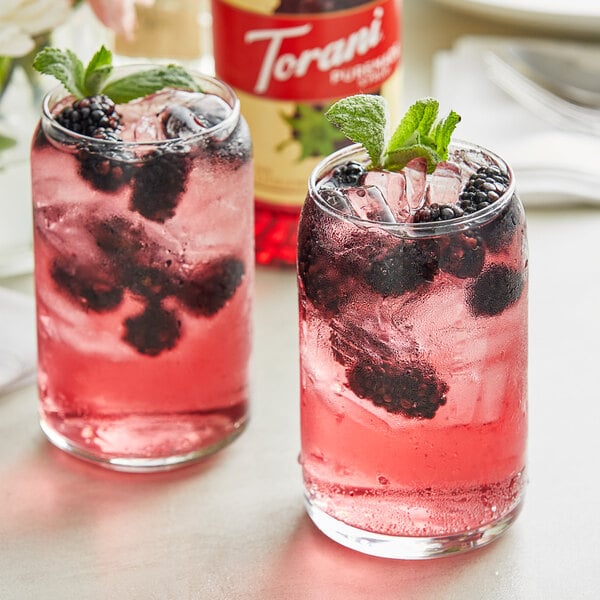 Two glasses of pink blackberry and mint drinks with berries.