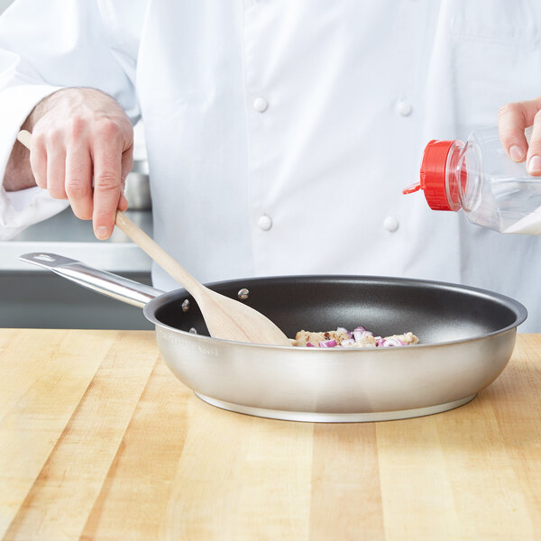 A chef stirring food in a Vollrath Centurion stainless steel fry pan with a wooden spoon.