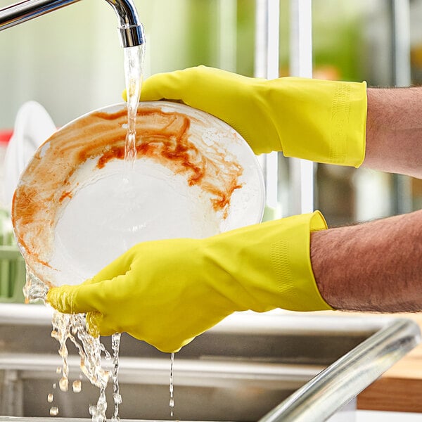 A person wearing yellow Lavex latex gloves washing a plate.