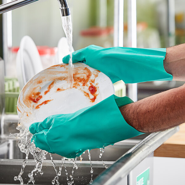 A person wearing Lavex green dishwashing gloves washing a plate under running water.