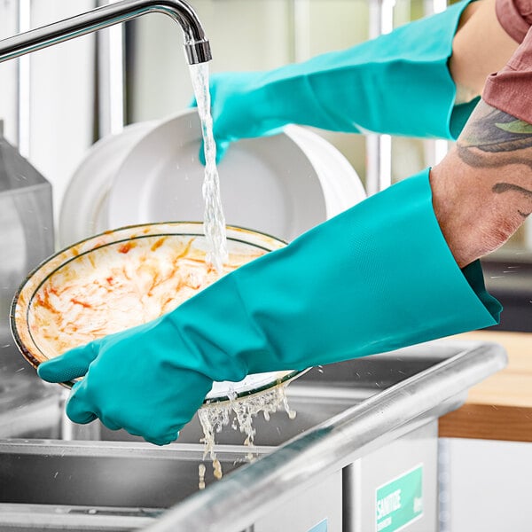 A person wearing Lavex small green nitrile gloves washing dishes under a faucet.
