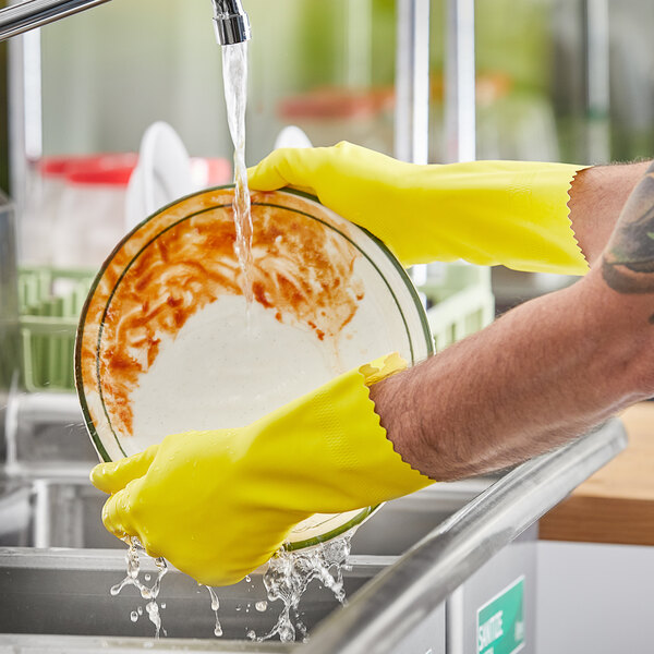 A person wearing yellow Lavex rubber gloves washing dishes in a sink.
